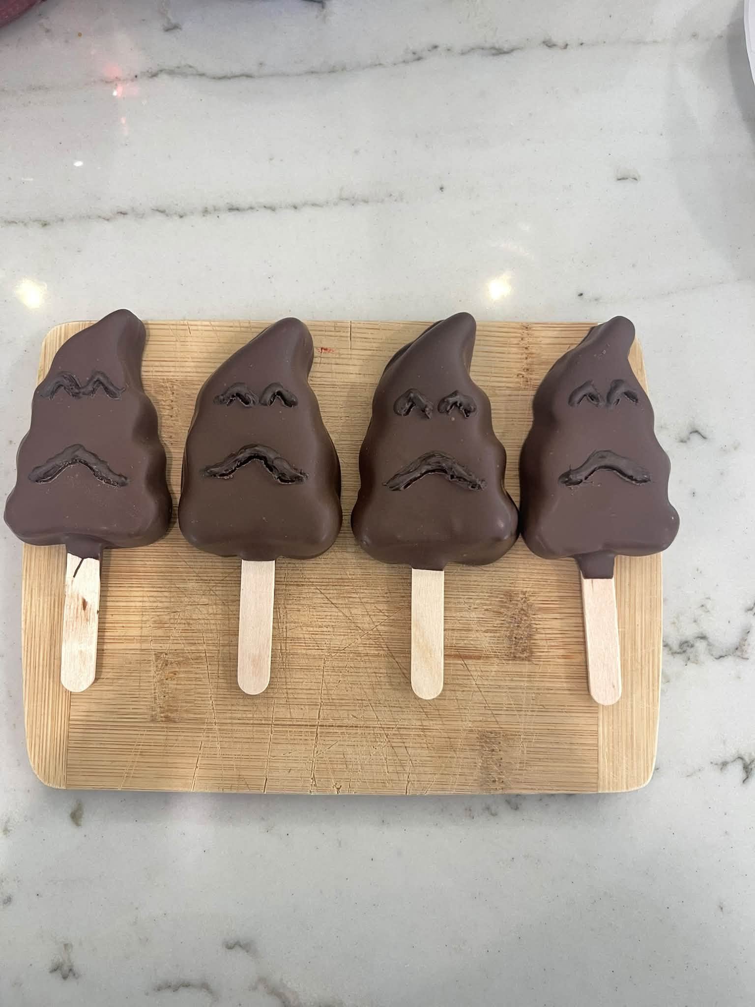 Chocolate-dipped treats on sticks arranged on a wooden board