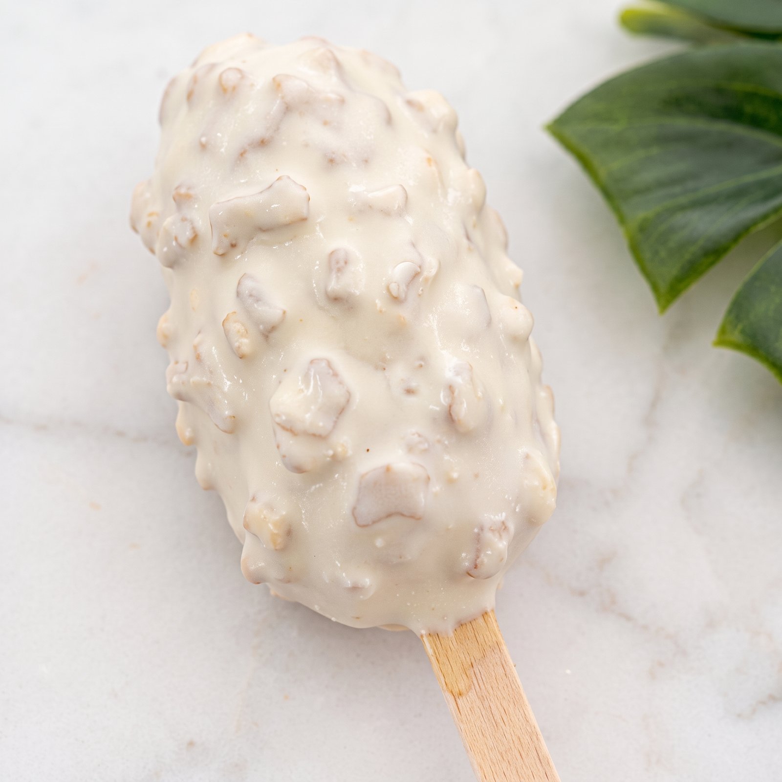 A white chocolate cakesicle with a crunchy coating