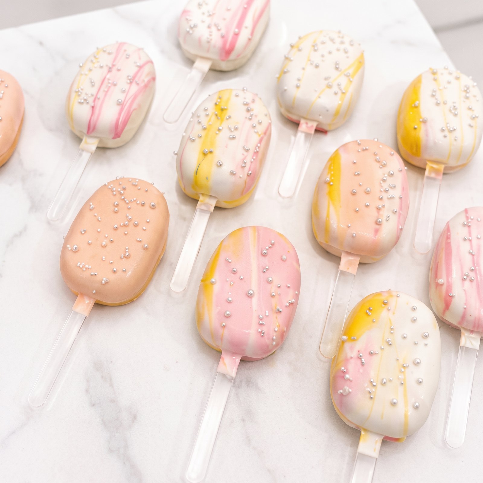 Pink and peach cakesicles lined up on white marble