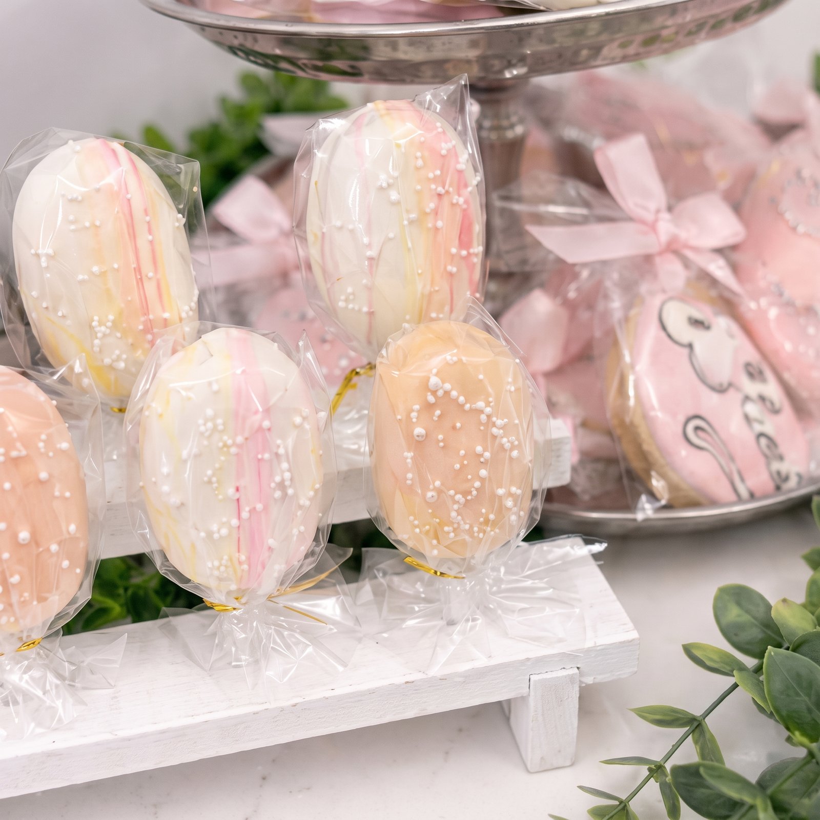 Wrapped cakesicles on a display stand with greenery