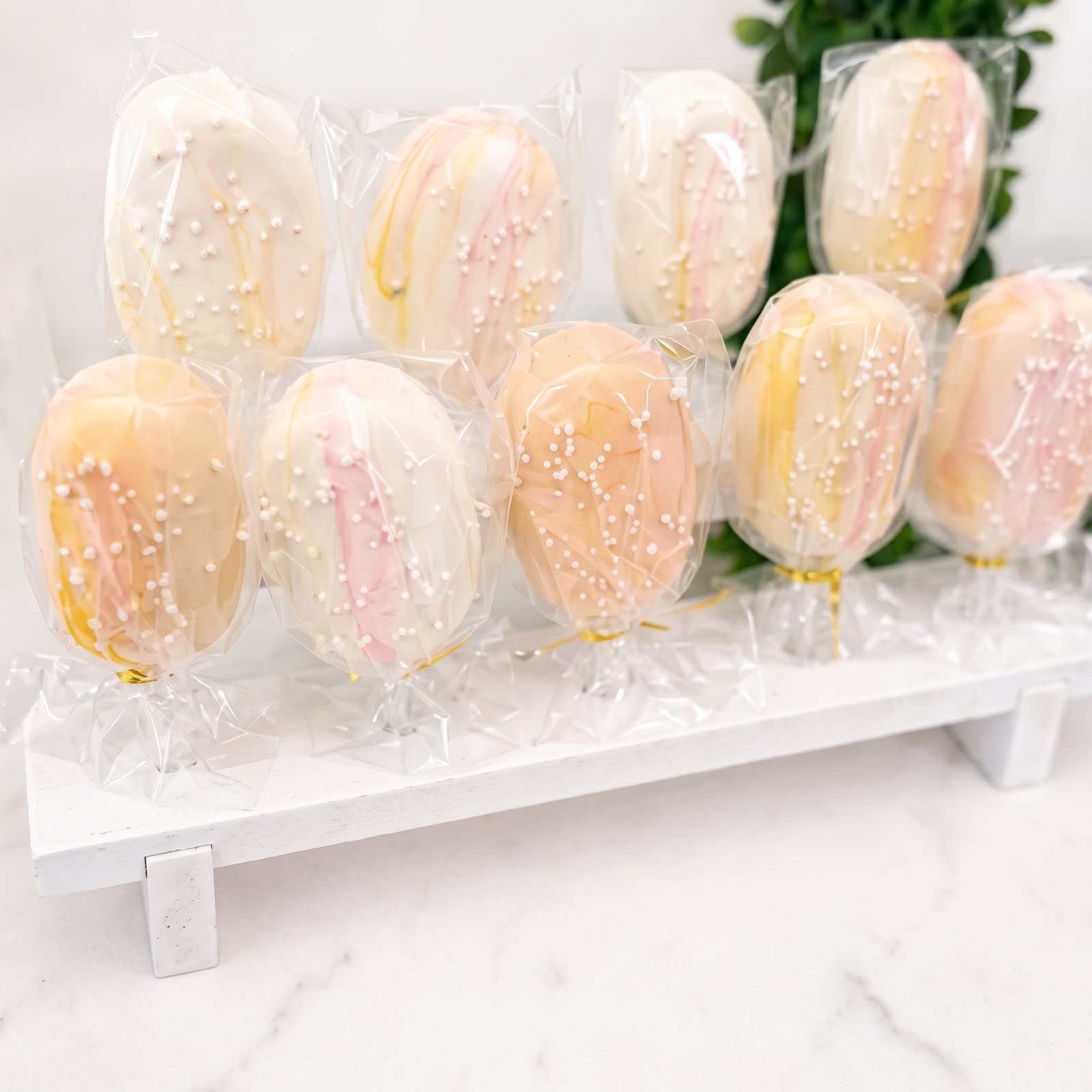 Wrapped pastel cakesicles on a white display stand
