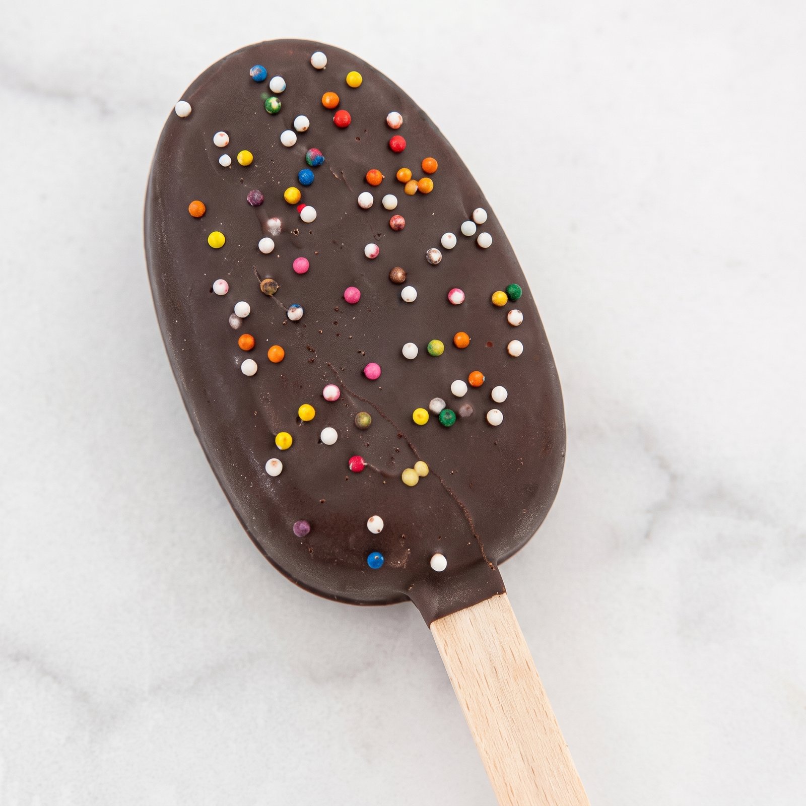 A chocolate cakesicle covered in rainbow sprinkles